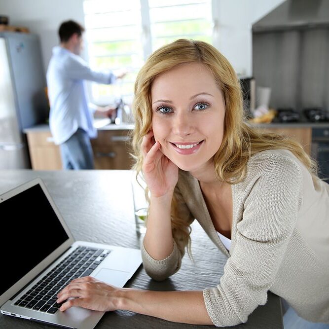 Cheerful blond girl connected on internet in home kitchen